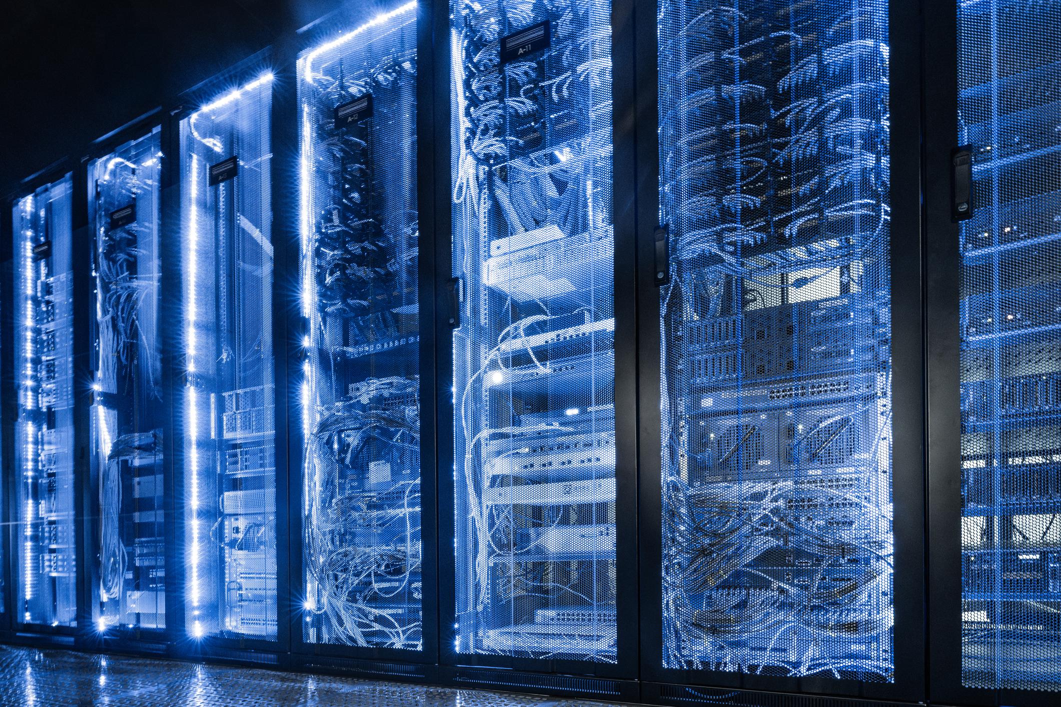 Ilustrasi data center cloud computing modern dengan server futuristik, chip AI pada motherboard, dan workstation teknologi berwarna biru.